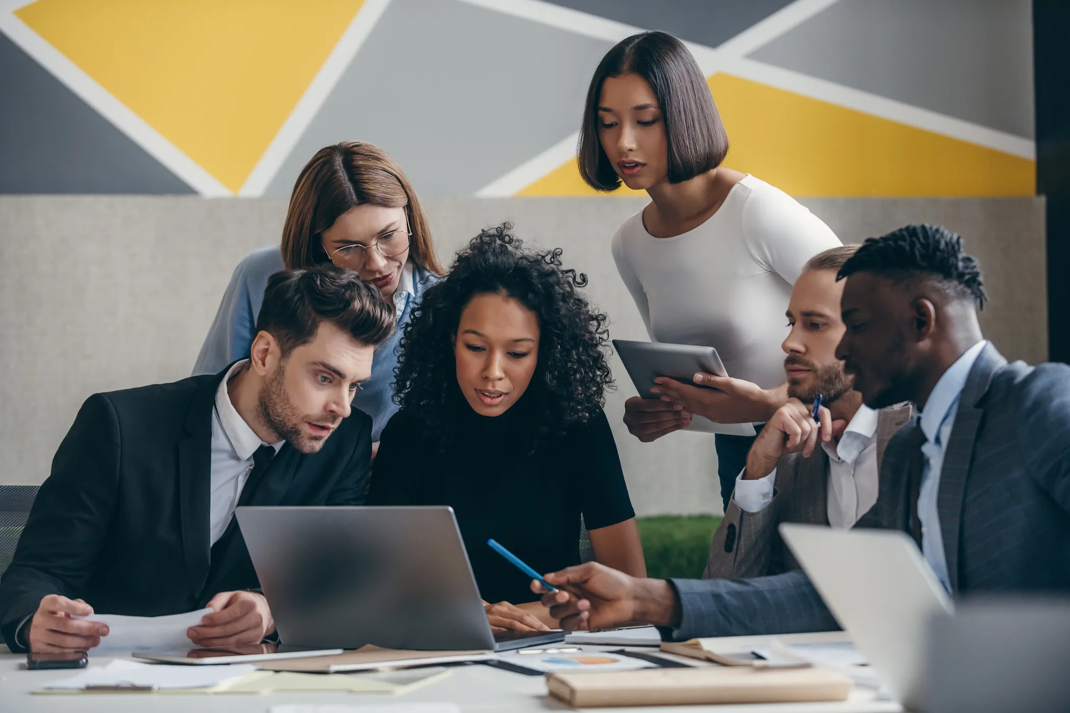 Diverse group of five colleagues crowded around a laptop in a modern office, representing the pressure and complexity of scaling drug discovery AI teams