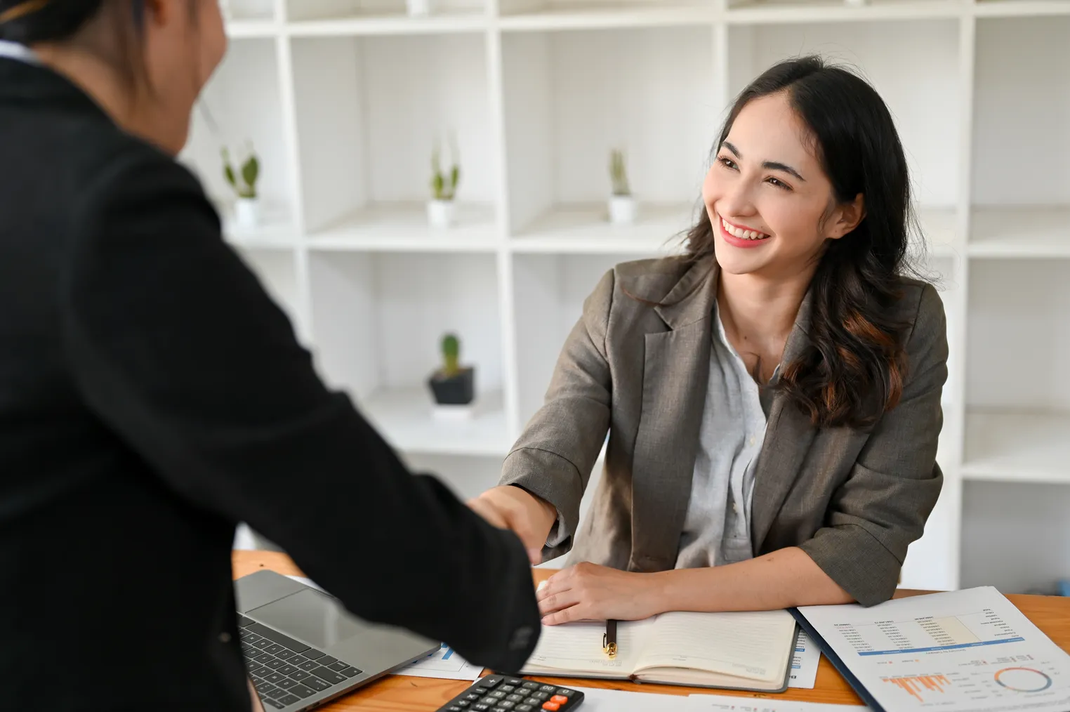 Professional woman in business attire shaking hands across a desk in a bright office setting, representing a successful career transition from FAANG to a new role