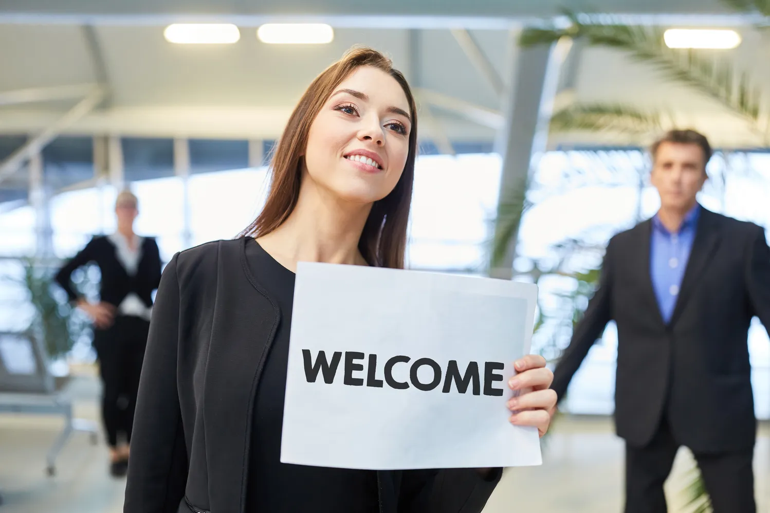 Professional holding a WELCOME sign in a bright office lobby, representing onboarding and new employee arrival for drug discovery AI teams