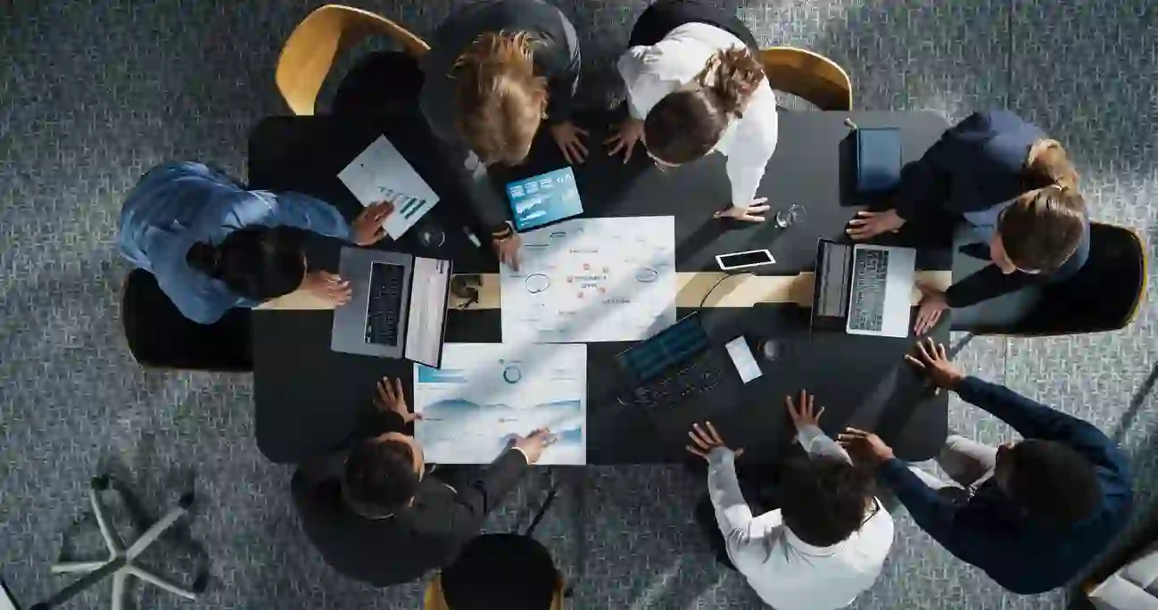 Diverse team collaborating around a boardroom table with laptops and documents
