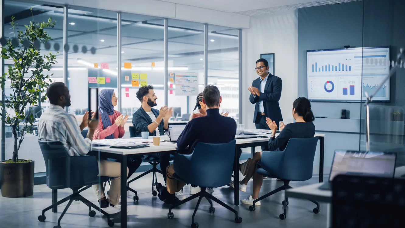 Diverse and international team applauding a presenter in a modern boardroom, representing the evaluation of AI, ML and data science professionals