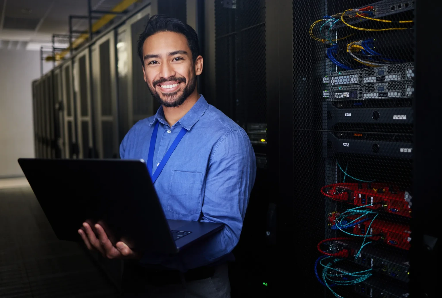 Confident professional man smiling with laptop in a modern server room