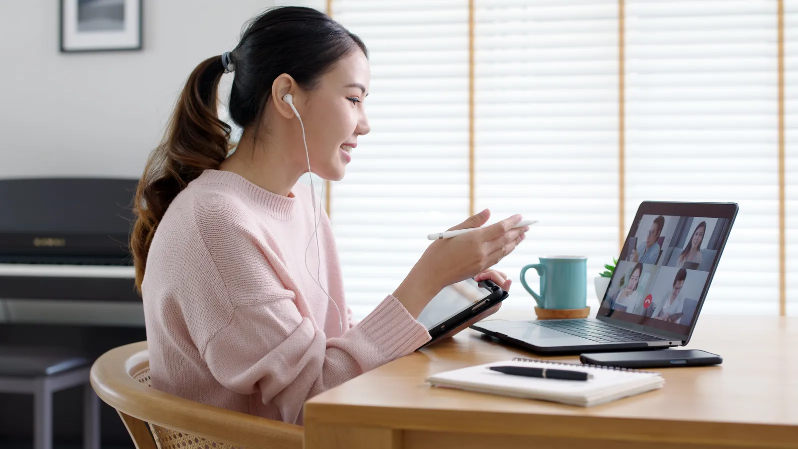 Woman smiling on a video call at a bright home desk, managing remote team