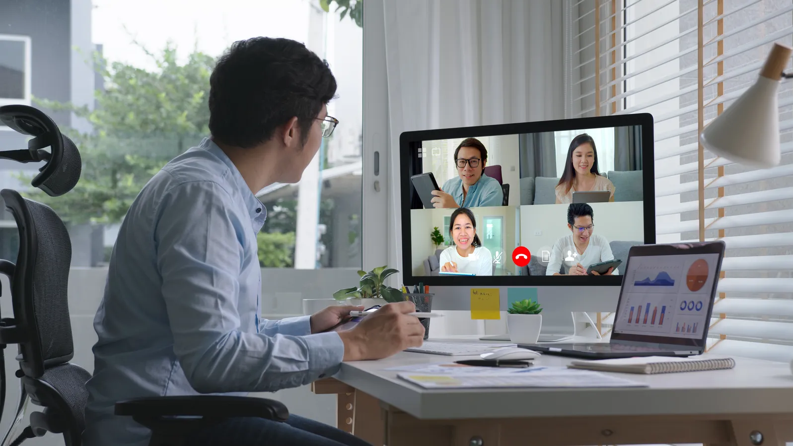 Man on a video call at home desk with data charts visible, working remotely
